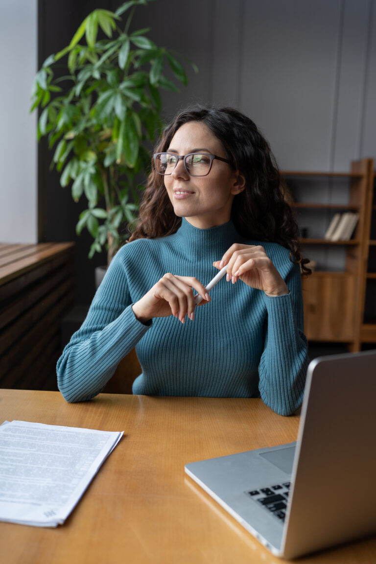 Smiling happy female employee at workplace looking in window and dreaming during work time